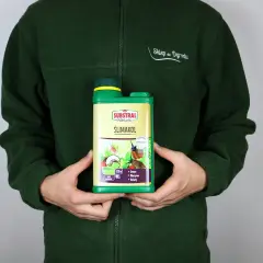 Osoba w zielonej bluzie trzyma butelkę preparatu ŚLIMAKOL, który chroni rośliny przed ślimakami.