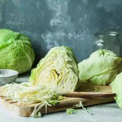 Świeża kapusta, gotowa do kiszenia. Widać całe główki, przekrojoną na pół oraz poszatkowaną, co sugeruje domową uprawę i przygotowanie.