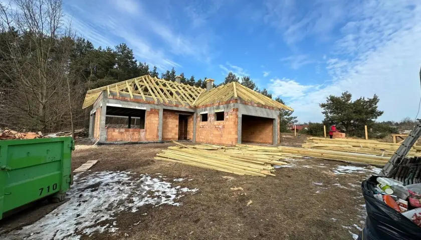 Budowa domu z cegły, widoczne drewniane elementy konstrukcji dachu i materiały budowlane.
