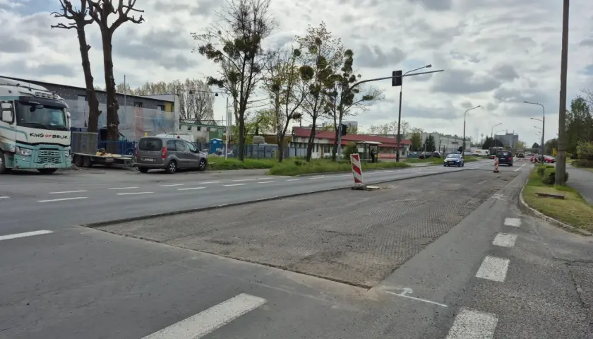 Droga w Opolu z widocznymi pracami drogowymi, samochodami i drzewami.